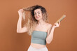 © New Africa - Unhappy woman trying to brush her tangled hair on brown background