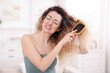 © New Africa - Unhappy woman trying to brush her tangled hair at home
