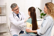 © New Africa - Endocrinologist in medical gloves and glasses examining girl's thyroid gland while her smiling mother supporting her on chair in clinic