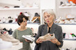 © JackF - In shoe store, young woman admires cool design of trendy model of snickers and shows them to elderly mother. Female clients want buy and choose jogging shoes