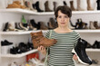 © JackF - Woman holds sample of shoes, chooses shoes in store. Female buyer examines autumn shoes with laces, twirls them in hands.