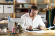 © caftor - Middle-aged male dressmaker wearing earphones drawing on tablet in sewing workshop