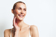 © SHOTPRIME STUDIO - Smiling woman with clear skin looking away, natural light on face, minimal makeup, white background, relaxed expression, bare shoulders, healthy complexion