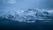 © AmazingAerialAgency - Aerial view of snow-laden peaks meet the frigid waters, creating a stark contrast in the muted light, Hamn, Troms, Norway.