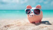 © KotBaton - Piggy bank with sunglasses standing on sandy beach, ocean background, concept of travel savings, summer budget and vacation planning