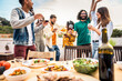 © Davide Angelini - Group of young people having fun drinking red wine on balcony rooftop bbq dinner party - Happy multiracial friends eating barbecue food at restaurant terrace - Food and drink life style concept