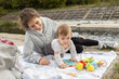 © Anna - Cute young mother plays with little baby while sitting on blanket in park. Happy Mother's Day. Tender maternal feelings. joy of motherhood, emotional moments with child. Children's games outdoors.