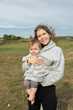 © Anna - cute young mother plays with her little barefoot baby, tucked under her hoodie. Happy Mother's Day. Tender maternal feelings. The joy of motherhood, funny moments with child