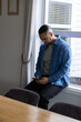 © wavebreak3 - Man sitting on window ledge using smartphone in dining nook with wooden table wearing denim jacket