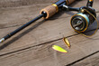 © Denis Kadatsky - A spinning rod with a reel and fishing lures lies on an old wooden table.