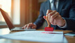 © Pete - Man in suit stamps paper document with red stamp near laptop. Official approves paperwork for business, legal contract or permit validation.