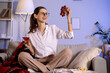 © Pixel-Shot - Beautiful young happy woman with glass of red wine and grapes sitting on sofa in evening at home