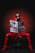 © Pixel-Shot - Beautiful young fashionable woman in trendy outfit reading newspaper sitting on chair against burgundy background