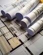 © Bat-Studio - Architectural Blueprints: A close-up shot revealing a collection of architectural blueprints rolled and spread out, showcasing intricate details.