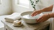© s2rd studio images - Minimalist self-care scene with hands gently touching water in a ceramic bowl, soft natural light, soap, and linen, creating a calm and soothing wellness atmosphere.