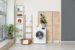 © Pixel-Shot - Modern washing machine with basket, shelving unit and dressing screen near white wall. Interior of home laundry room