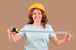 © Pixel-Shot - Female construction worker with measuring tape on beige background