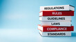 © maman - A stack of books about regulations, rules, and compliance on a blue background
