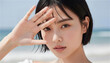 © Yka - 手で日差しを遮りながら海辺に立つ若い女性