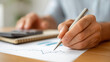 © Denis Yevtekhov - Faceless close-up of business strategy hands sketching a rising financial chart on bright paper with a marker, surrounded by a calculator and notebook, growth plan, financial management,