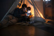© Westend61 - Father and son reading on tablet in cozy tent at home at night