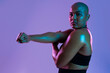 © Westend61 - Bald athlete in sportswear stretching arm in studio with purple background