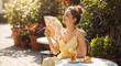 © NeuroCake - Happy young woman cooling herself with a folding fan at a cafe. Female relaxing with iced tea and a croissant on a hot summer day