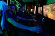 © .shock - Competitive Gamers Playing Multiplayer Shooter on PCs in Neon-Lit Gaming Arena With Headsets and Keyboards