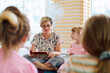© .shock - Female teacher reading a picture book to preschool children during storytime in a bright classroom