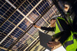 © ultramansk - Technician inspects solar panels under a large solar carport structure. Focused on clean energy, and sustainability, Engineer in safety vest and helmet pointing towards a solar powered carport.