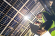 © ultramansk - Technician inspects solar panels under a large solar carport structure. Focused on clean energy, and sustainability, Engineer in safety vest and helmet pointing towards a solar powered carport.