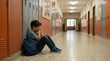 © mashimara - Young boy sitting alone in a school hallway, covering his face in distress