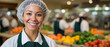 © Olga Ко - Smiling female food service worker in apron and hairnet, blurred school cafeteria with fresh healthy food in background.