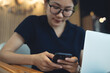 © tippapatt - Young asian woman using mobile phone and laptop remote working at cafe, freelance at work, digital nomad lifestyle, online business concept