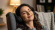 © KAMRAN - Happy relaxed woman listening to music with headphones on living room couch perfect for comfortable domestic weekend leisure
