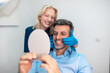 © Graphicroyalty - Happy man looking in mirror after dental treatment with female dentist. Patient satisfied with white teeth and smile in clinic. Aesthetic dentistry, veneers and professional healthcare concept.