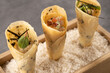 Three gourmet sushi cones filled with fresh seafood and garnished with herbs, presented on a bed of rice in a wooden serving tray