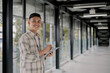 © Rijjal - Young asian man smiles while writing on tablet beside large glass window. Working outdoor. Chilling Outside, Urban life.
