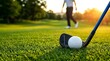 © Ada - Close-up of a white golf ball and black iron club on lush green grass at sunset with a blurred golfer walking in the background on a luxury golf course during golden hour.