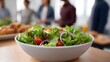 © Thares2020 - A vibrant fresh salad served in a white bowl set against the backdrop of people in a modern meeting environment