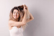 © New Africa - Unhappy woman trying to brush her tangled hair on light grey background, space for text