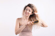 © New Africa - Unhappy woman trying to brush her tangled hair on light grey background
