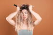 © New Africa - Unhappy woman trying to brush her tangled hair on brown background