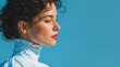 © NeuroCake - Profile portrait of a young woman with curly hair. Female model with red lipstick and white ruffled blouse against a blue backdrop