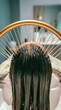 © Sergei - Vertical close-up of long dark wet hair being washed with a golden halo water ring. Head spa scalp treatment in a modern salon