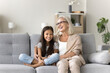 © fizkes - Cute school-age girl spend time with older granny, multigenerational family siting on couch, laughing, lead pleasant, trustworthy conversation, share news, joking, enjoy carefree rest at home together