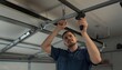 © Masaji - A skilled male technician or handyman is diligently working to repair a residential garage door opener mechanism.