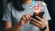 © Kunal - Person holds a smartphone while popular social media application icons float above the screen.