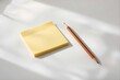 © Z9 - 木漏れ日が差し込む白いデスクに置かれた真っ新な黄色の付箋と鉛筆、新しいアイデアや計画を象徴するビジネス・教育背景素材（コピースペース・知的・ミニマル）