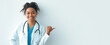 © Prostock-studio - A woman wearing a white coat and a stethoscope smiles at the camera. She stands against a light wall and points to the side.